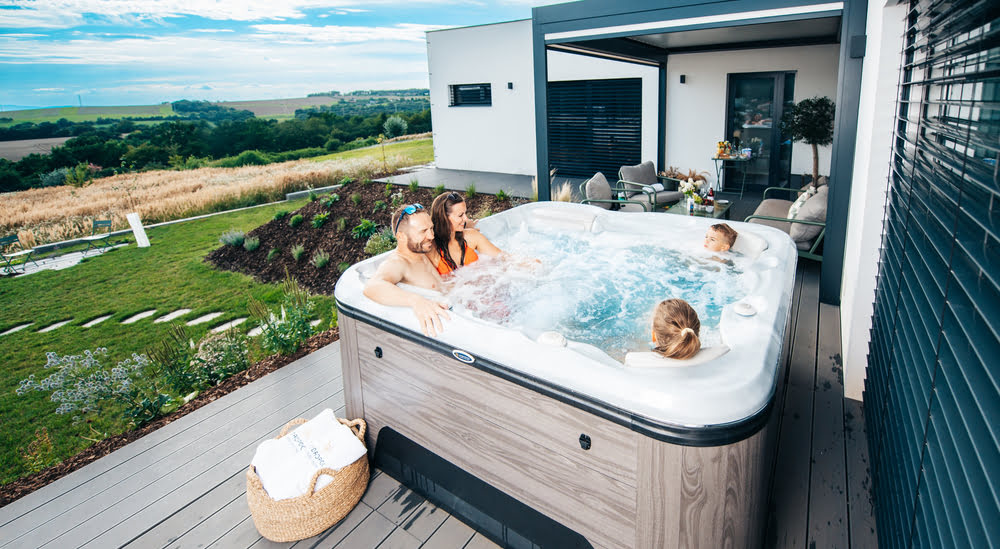 Bain-bouillonnant-et-spa-quelles-differences Une famille se détend dans un spa installé contre leur maison avec vue sur le jardin.